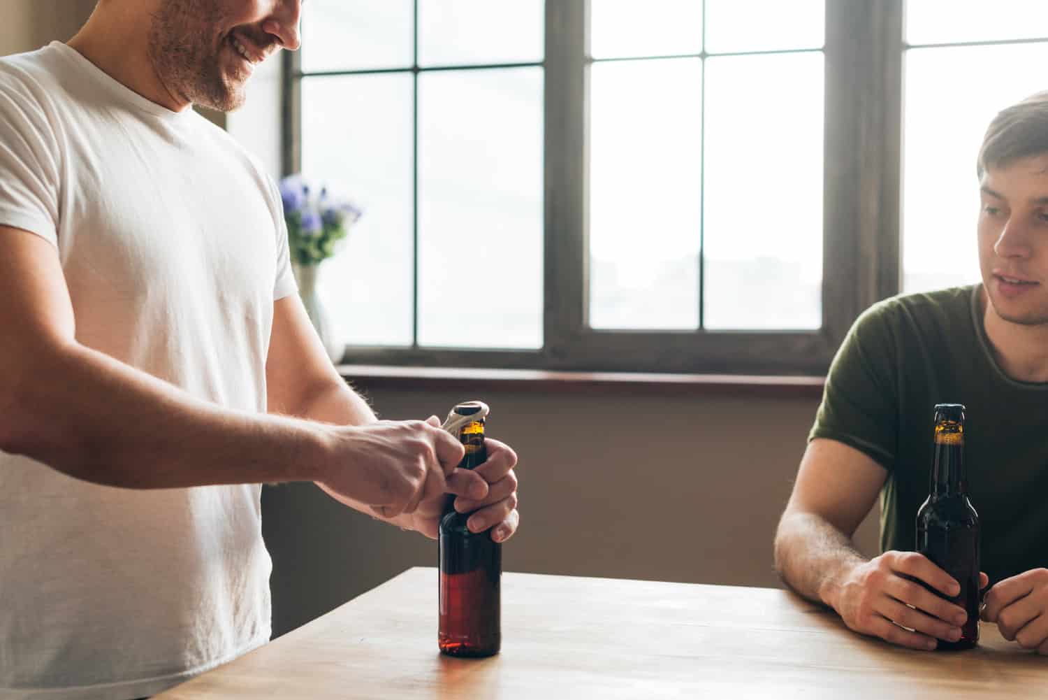 Man looking at his friend opening the Alcohol bottle with opener on table