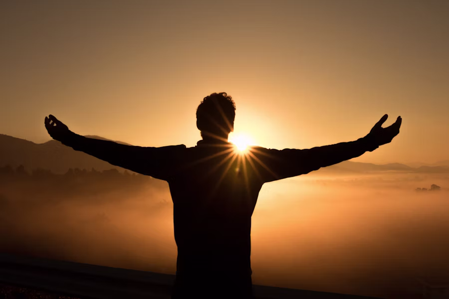 Person quietly reflecting near a window at sunrise